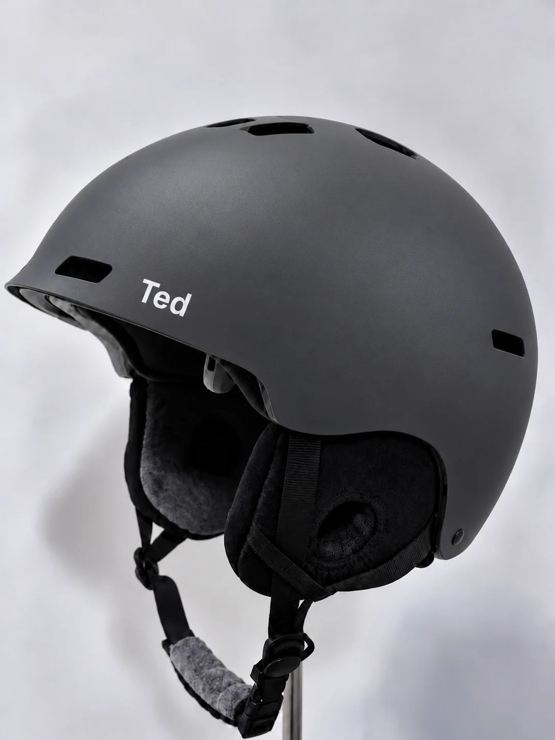 A plain charcoal skate helmet on a stand with only the name Ted in small white letters on the side